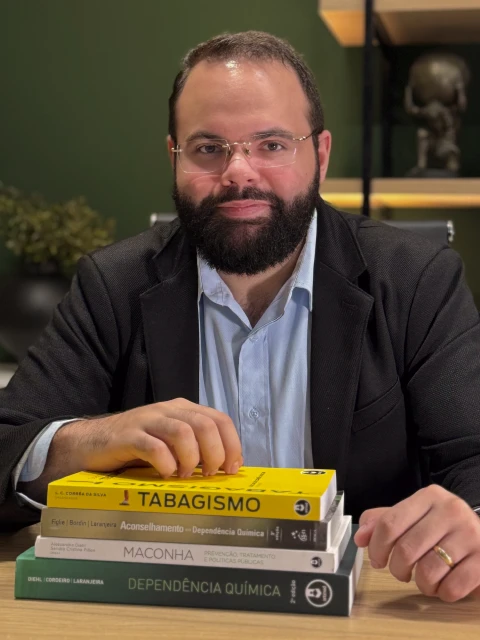 Marques Júnior em seu consultório, com livros sobre dependência química sobre a mesa